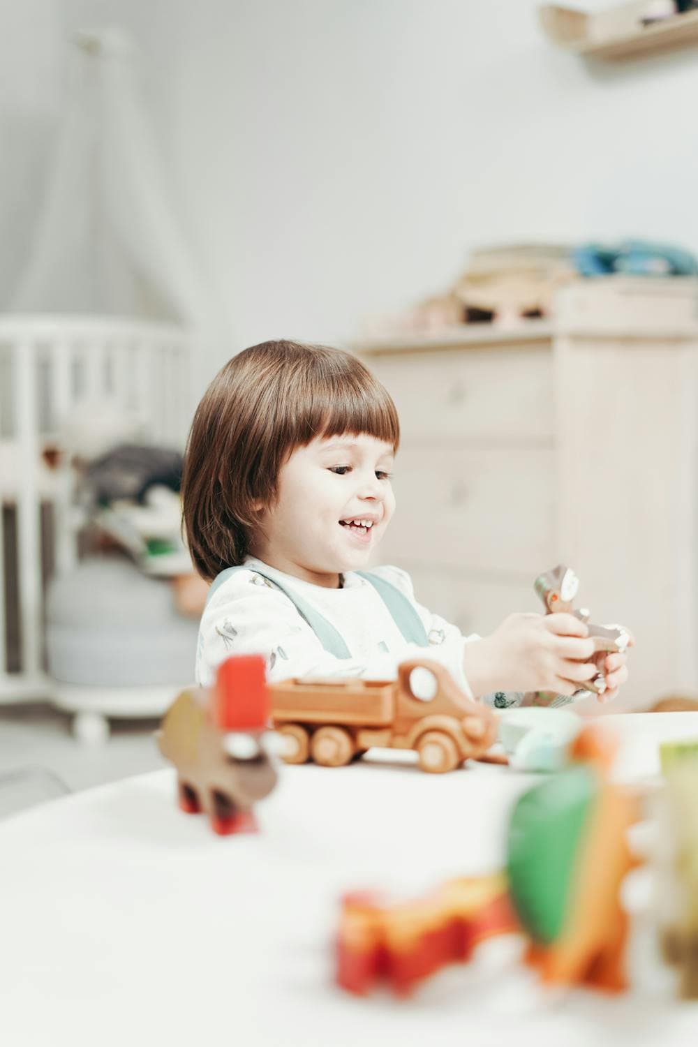 Smiling preschooler playing with wooden toy animals and a toy truck at a table