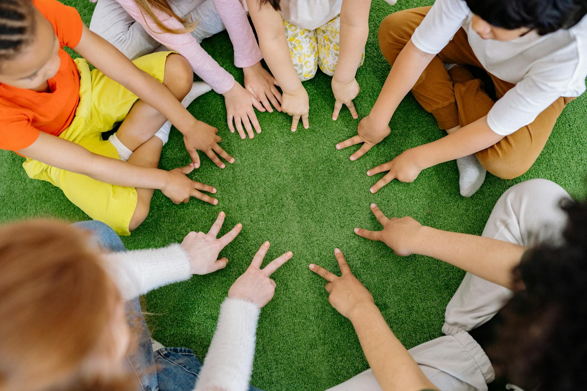 Children sitting in a circle playing outdoor games together on green grass